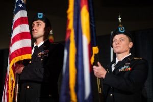 Two individuals in military uniforms holding the American flag