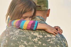 Little female child is hugging a soldier. Close up portrait of happy girl is hugging her father in military uniform.