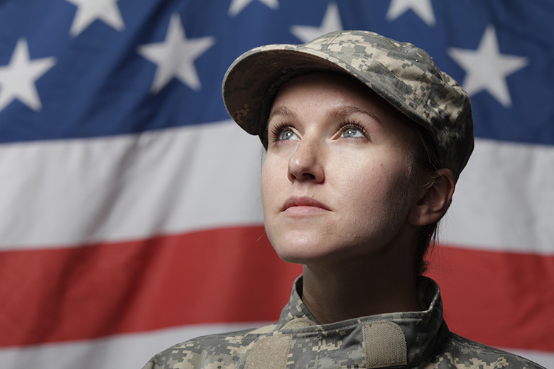 Photo of a female soldier in uniform standing in front of an American flag and looking into the distance