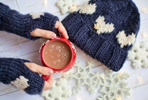 Picture showing a person's hands wearing mittens and holding a mug of hot chocolate