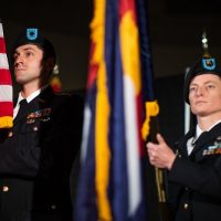 Two individuals in military uniforms holding the American flag