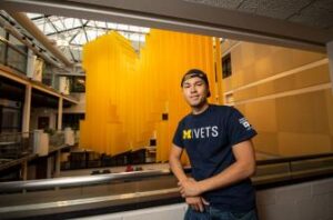 Image of University of Michigan's PAVE Team member, Dominic Petersen in front of a large block M.