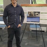 Figure with hands in pockets standing in front of a poster presentation and smiling.