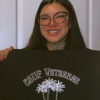 Smiling figure holding up a t-shirt reading "CSUF Veterans"