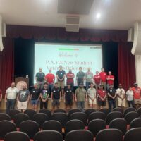 Group of people standing in 2 lines on a stage in front of a projector screen reading: "PAVE New Student Veteran Orientation"
