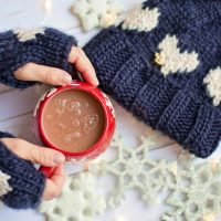 Picture showing a person's hands wearing mittens and holding a mug of hot chocolate